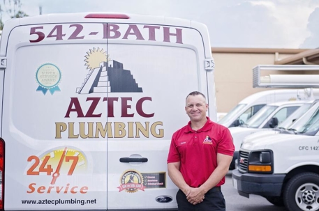 back of Aztec Plumbing van with employee standing next to it