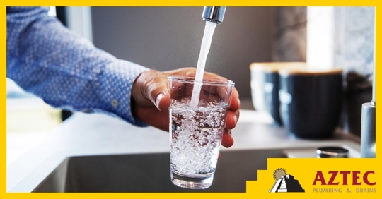 A person holding a glass of water being filled by a faucet