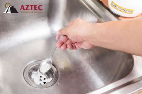 stainless steel sink with someone putting baking soda down drain to clean