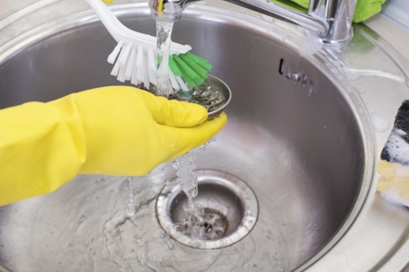 Homeowner clearing kitchen sink with gloves