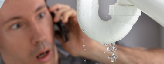 worried man looking at leaking sink pipe